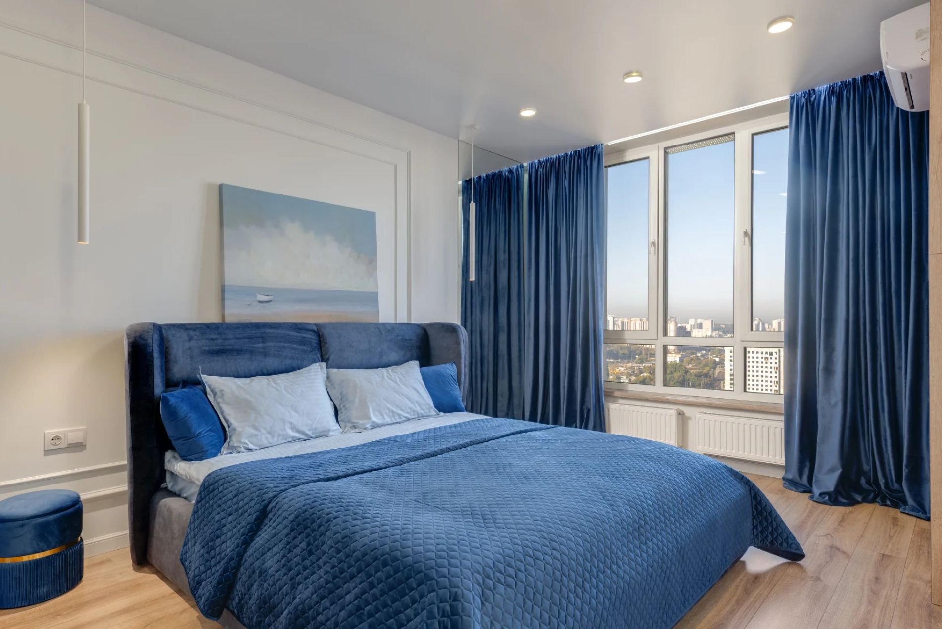 Bedroom Remodeling Modern bedroom with blue bedding, blue curtains, large window, city view, and soft lighting.