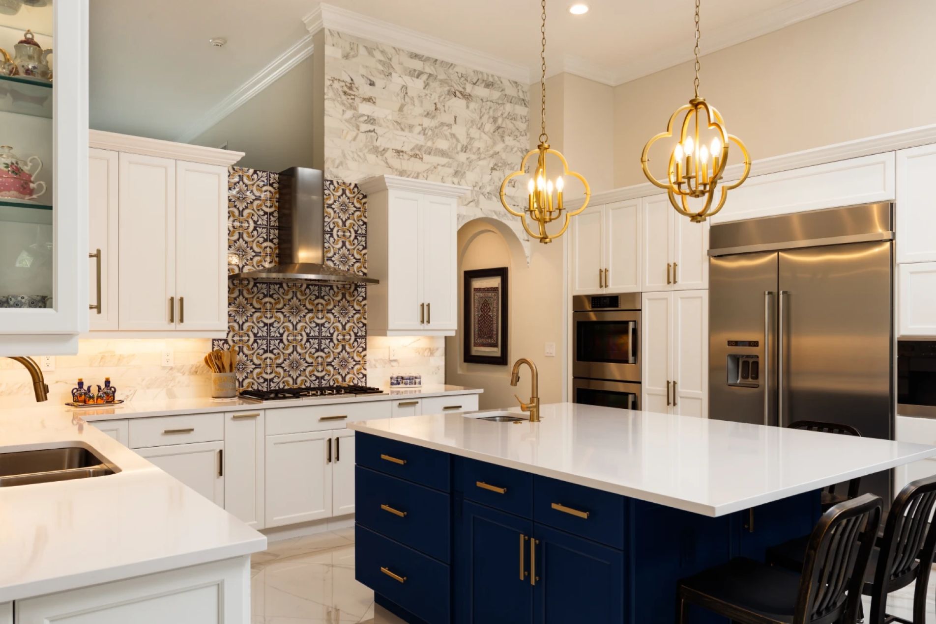 Kitchen Remodeling Modern kitchen with white cabinets, blue island, gold fixtures, stainless appliances, and patterned backsplash.
