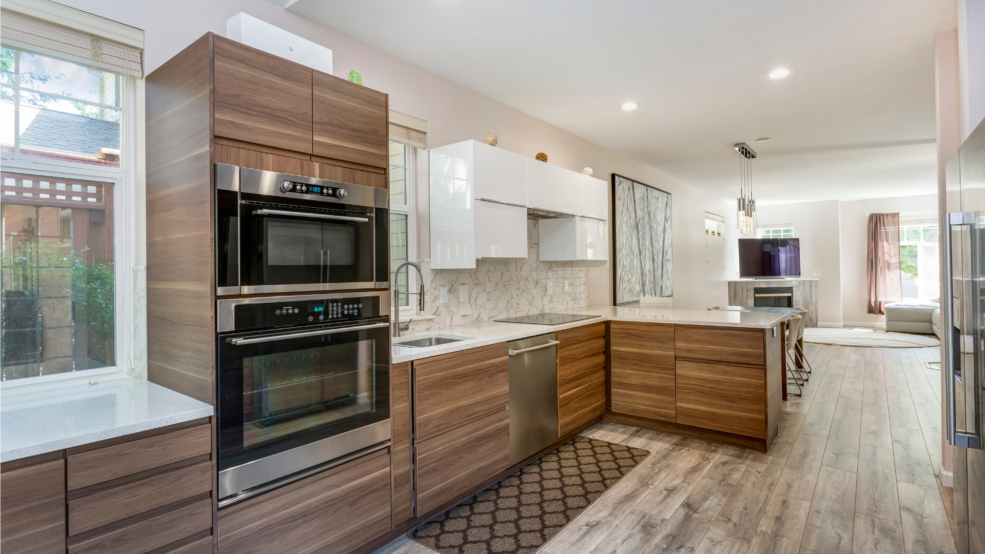 Modern kitchen with wood cabinets, stainless steel appliances, and white countertops, leading to a dining area.